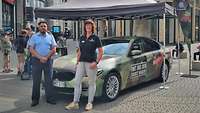 Zwei Personen vor einem folierten Dienstwagen der Bundeswehr in der Kölner Fußgängerzone
