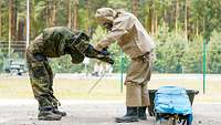 Ein Soldat zieht einem anderen Soldaten den Schutzanzug aus. 