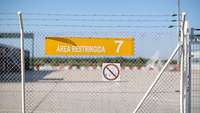 Vor einem Teil der Air Base befindet sich im Vordergrund ein Zaun, auf dem in Spanisch das Wort „Sperrgebiet“ steht. 