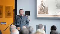 Soldat steht vor einer sitzenden Menschengruppe an einem Rednerpult.