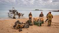 Soldaten tragen Rücksäcke und Kartons von einer kleinen Fähre, die am Strand liegt.