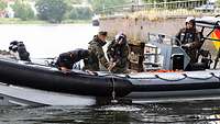 Zwei Soldaten ziehen einen Gegenstand aus dem Wasser in ein Schlauchboot.