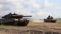 Zwei Leopard-Panzer befinden sich auf einer Anhöhe. Der hintere ist bereits losgefahren.