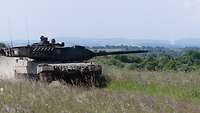 Ein Leopard-Panzer fährt über eine Wiese. Sein Turm ist nach links gerichtet.