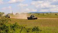 Zwei Panzer durchqueren eine steppen ähnliche Landschaft und wirbeln dabei Staub in die Luft auf
