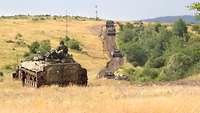 Ein Schützenpanzer BMP steht auf einer offenen Graspläne. Daneben und im Hintergrund fahren Panzer. 