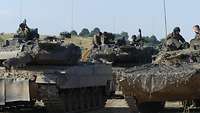 Leopard 2 Panzer und BMP Schützenpanzer stehen nebeneinander. Ihre Besatzungen sind aufgesessen. 