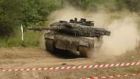 Minen liegen auf dem Boden. Sie sind mit rot-weißem Leuchtband markiert. Ein Panzer fährt an dem Minenfeld vorbei. 