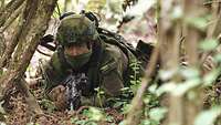 Ein tschechischer Soldat liegt auf dem Waldboden. Er hat seine Waffe im Anschlag.