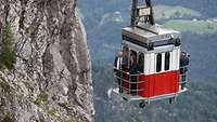 Zwei Männer stehen auf der Veranda von einer Gondel, die auf einen Berg hochfährt. 