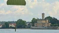 Ein Fallschirmspringer kurz vor der Landung im Wasser, im Hintergrund Gebäude am Ufer