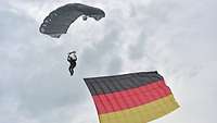 Ein Fallschirmspringer schwebt mit seinem Fallschirm zu Boden, an ihm weht eine Deutschlandflagge.