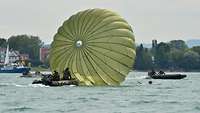 Ein Schlauchboot fährt in einen auf dem Wasser treibenden Fallschirm.