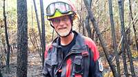 Andreas S. in Feuerwehruniform steht vor verbrannten Bäumen in einem Waldstück nach einem Einsatz.