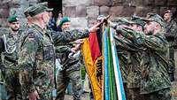Soldaten halten eine Hand auf die Fahnenstange, die von einem Soldaten waagerecht gehalten wird.