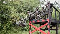 Soldaten stehen auf einem Podest und helfen einem Soldaten am Seil, das Wasserbecken zu überwinden.