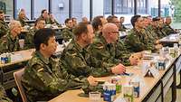 Teilnehmer der Veranstaltung in Uniform sitzen im Infanteriesaal und hören einem Vortragenden zu.