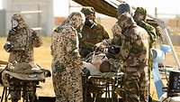 Mehrere Soldatinnen und Soldaten in Schutzausrüstung kümmern sich um eine Simulationspuppe auf einer Krankentrage.
