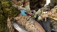Ein Soldat in ABC-Schutz zerschneidet die Hose des Patientensimulators