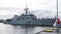 Ein graues Kriegsschiff vor einer Pier.
