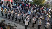 Soldaten stehen mit Blasinstrumenten an einer Hafenkante und spielen ein Lied.