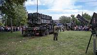 Ein LKW mit großen Boxen steht auf einer Wiese. Davor steht ein Soldat.