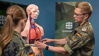 Zwei Soldaten stehen sich beim Interview gegenüber, ein Soldat zeigt dabei auf ein Anatomie Modell.