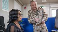 Ein Soldat und eine Frau in einem Büro schauen auf ein Papier, das der Soldat in der Hand hält.
