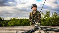Eine Person in deutscher Uniform klettert mit einem Sicherungssystem einen Turm hoch.
