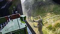 A person wearing a protective suit is holding a water lance, spraying down a green truck