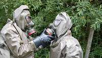 A person wearing a protective suit inserts the filter into the CBRN mask of another person wearing a protective suit