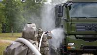 Two people in protective suits are spraying down a green truck with a white water hose