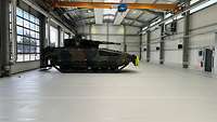 Ein kleinerer Panzer steht in einer Werkhalle, in der keine weiteren Maschinen zu sehen sind.