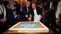 Ein Mann in Uniform und eine Frau schneiden eine große Torte an