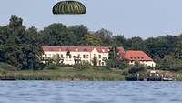 Ein Fallschirmspringer kurz vor der Landung im Wasser. Im Hintergrund ist ein Haus zusehen.