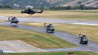 Vier NH-90 auf einem Flugplatz, die gemeinsam auf der Rollbahn ein „Abhebemanöver" durchführen