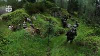 Mehrere Soldaten bewegen sich getarnt in einem stark bewachsenen Wald durch ein Pfad.