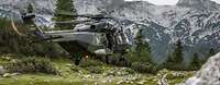 Ein NH-90 schwebt über eine Wiese zwischen den Alpen, dabei schaut ein Soldat aus der Seitentür.