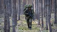 Soldaten mit getarnten Gefechtshelm mit Waffen marschieren im Wald hintereinander.