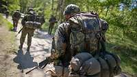 Soldaten marschieren in Schützenreihe mit schwerem Gepäck und bewaffnet durch den Wald.
