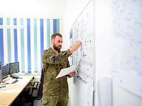 Büro- und Projektorganisation Ein Soldat steht im Büro neben seinem Schreibtisch und vor einem Whiteboard und bearbeitet den Bürokalender