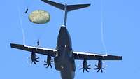 Unter blauem Himmel fliegt ein Flugzeug, während Soldaten herausspringen.