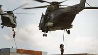 Zwei Hubschrauber schweben über zwei Dächern, an dicken Seilen rutschen Soldaten herunter.