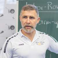 Ein Mann in Sportkleidung steht vor einer Tafel und erklärt etwas