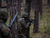 Ein Soldat steht mit seiner Waffe an einem Baum