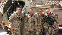 Vier Soldaten in Wüstenflecktarnanzug stehen vor einem beigen gepanzerten Fahrzeug in lockerer Pose. 