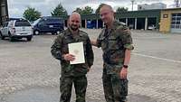 Ein Mann in Uniform überreicht einem jüngeren Mann in Uniform eine Urkunde.