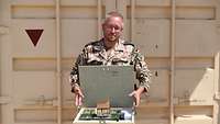 Ein Soldat steht vor einem Container und hält eine Holzkiste mit Munition darin in den Händen.