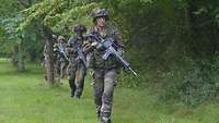 Soldaten bewaffnet mit Gewehren G36 gehen als Spähtrupp entlang einer Waldkante vor.