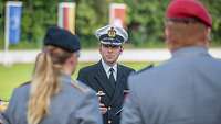 : Korvettenkapitän Robert A. steht auf dem Appellplatz. Hinter ihm wehen die Fahnen zur Kommandoübergabe 